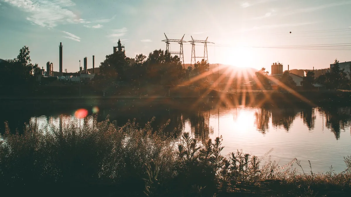 A captivating sunset over an industrial skyline reflected in a tranquil water body.